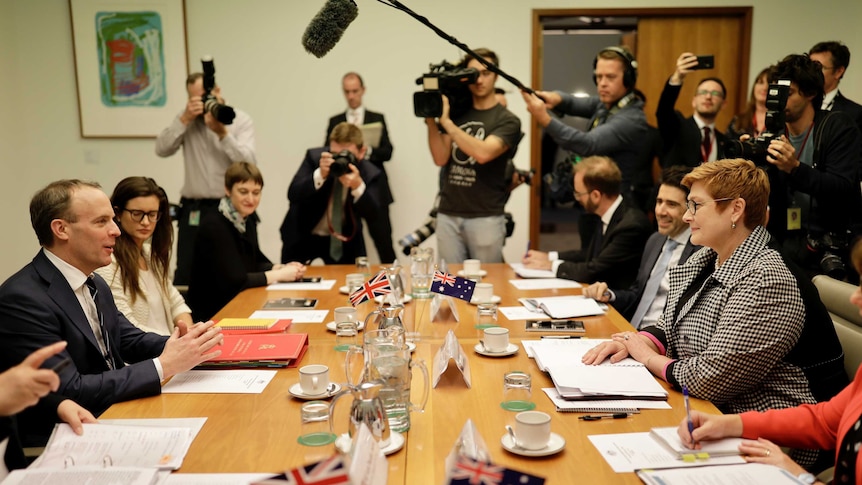 Dominic Raab and Marise Payne talk across a table surrounded by staffers and media