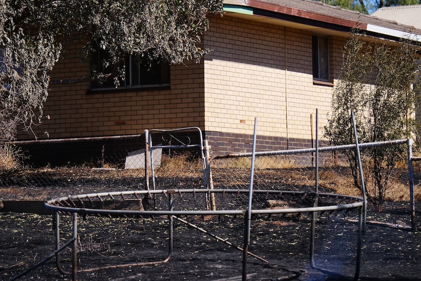burnt out trampoline with burnt black ground within a metre or two of a home