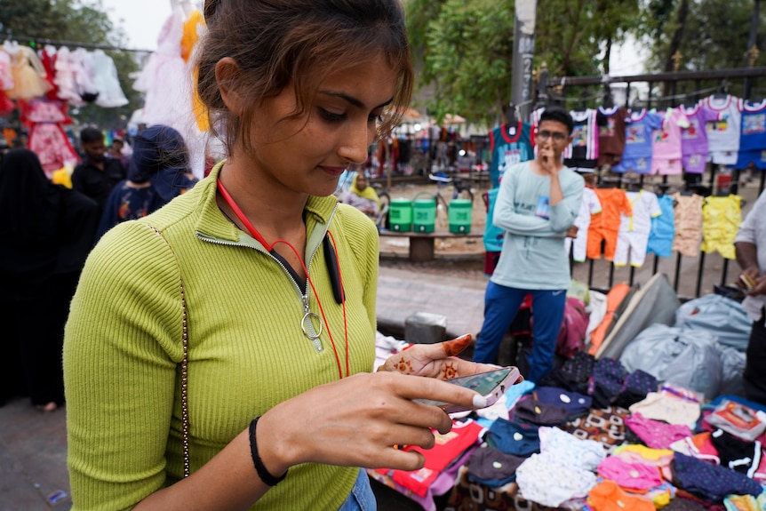 A young woman in a lime green top uses her phone in an open air market