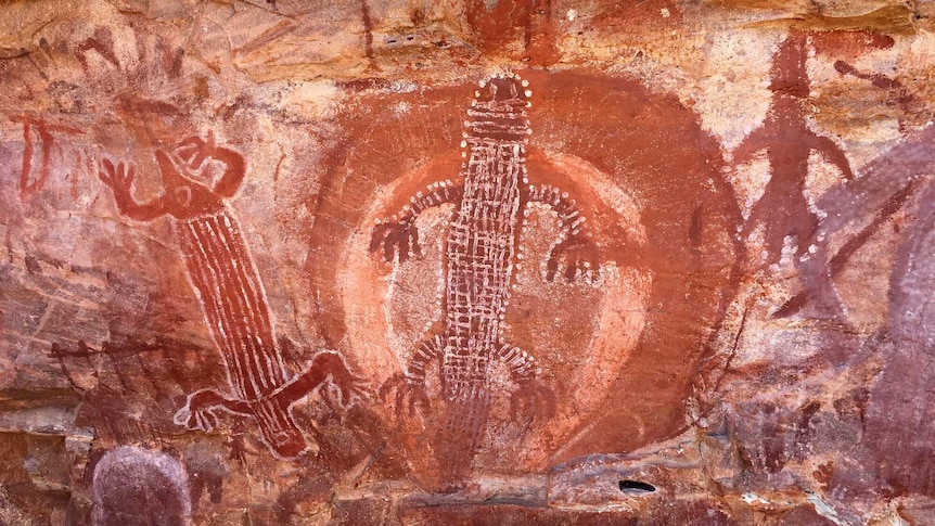 Indigenous rock art showing red animal figures on brown rock.