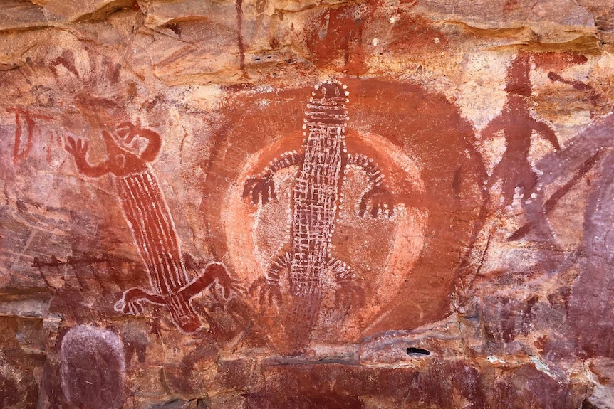 Indigenous rock art showing red animal figures on brown rock.