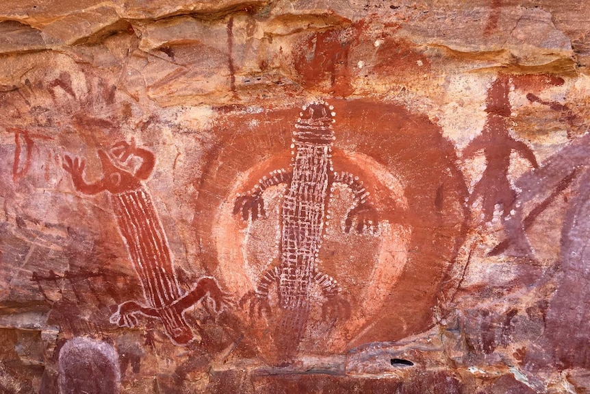 Indigenous rock art showing red animal figures on brown rock.