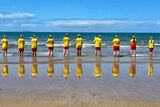 A dozen surf life savers stand looking at the ocean at Sarina. 