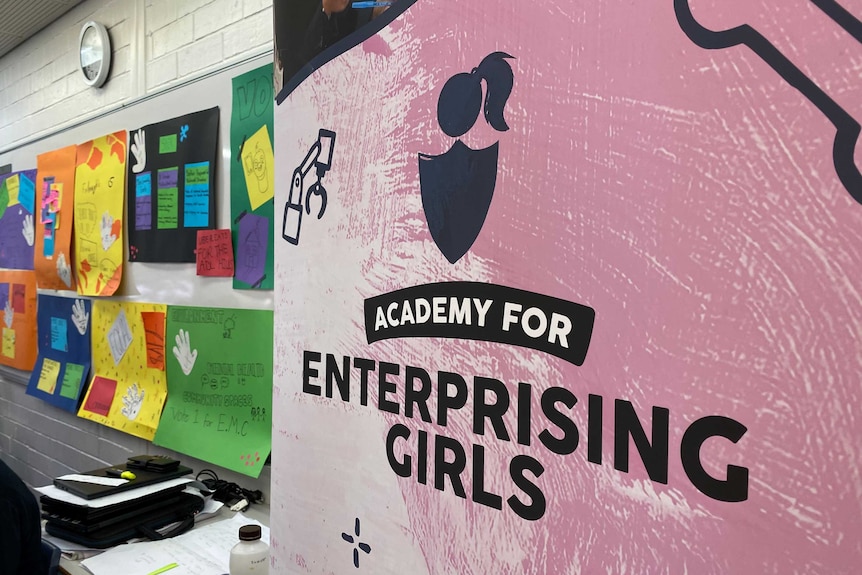 A pink and white sign for the academy for enterprising girls in a classroom.