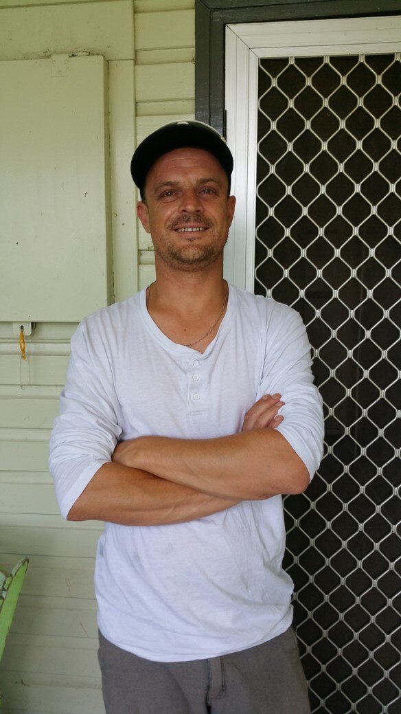 Man in black cap and white shirt smiles at the camera 