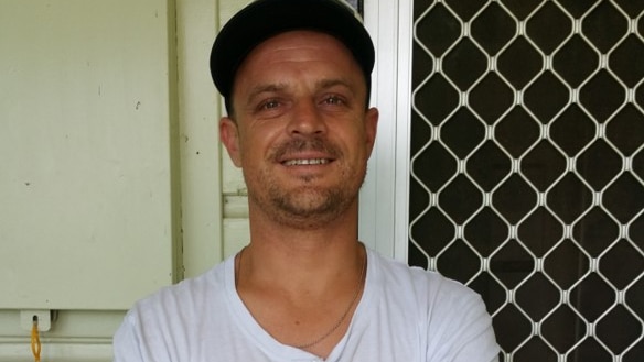 Man in black cap and white shirt smiles at the camera.