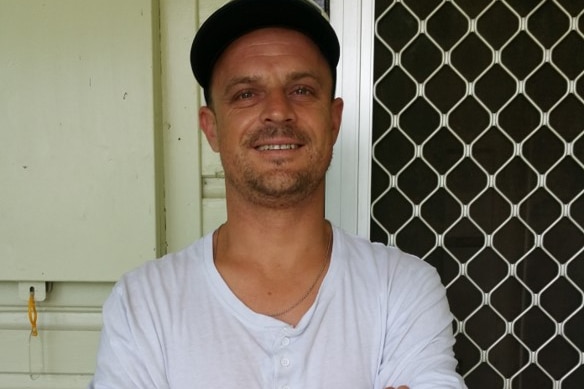 Man in black cap and white shirt smiles at the camera 