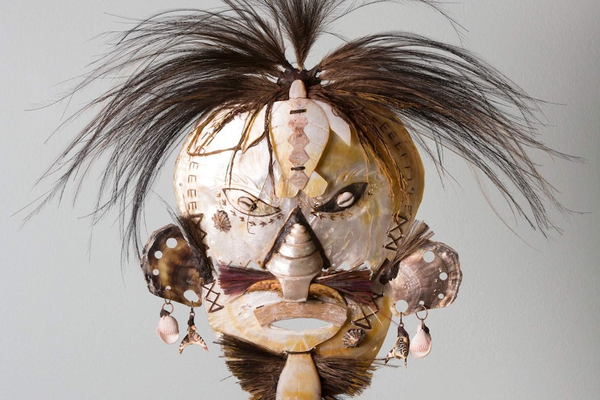 A tribal mask with brown hair strands sticking out of the top.