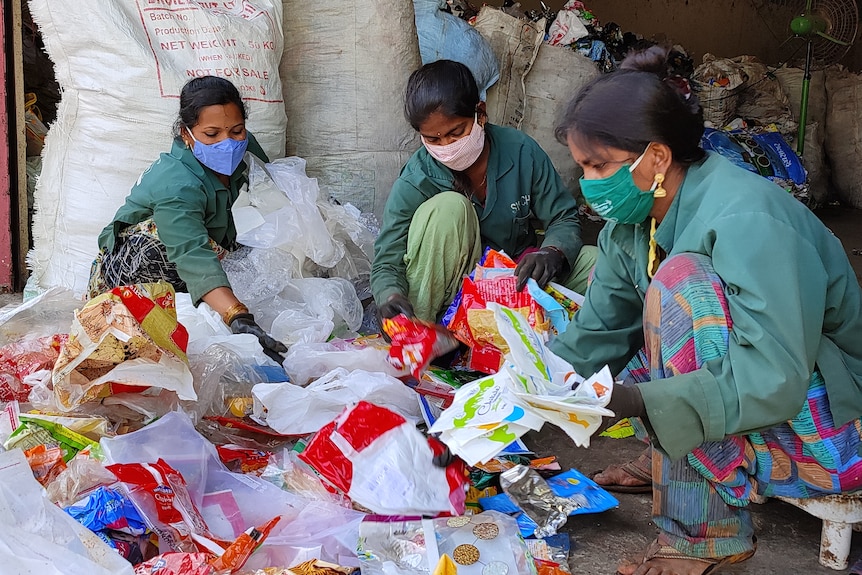 Three Indian women in workers uniforms sort through plastics.  