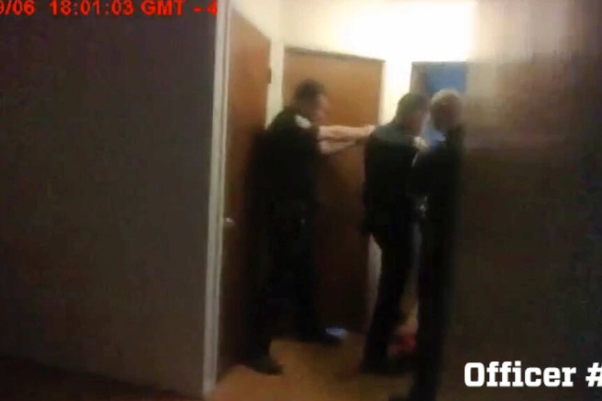 Three police officers are seen in body camera footage pointing their guns through a doorway.
