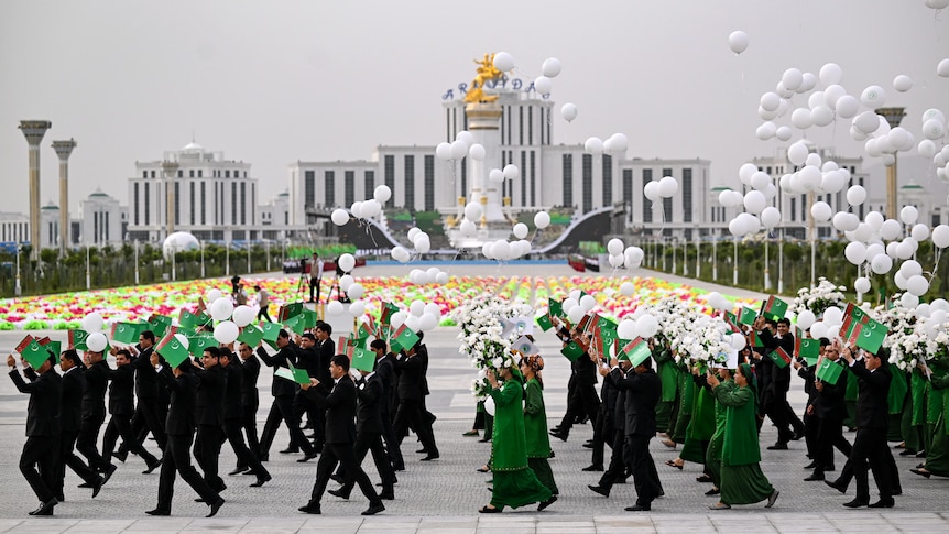 Participants parade with Turkmen flags, artificial flowers and white balloons in front of a new, white city.