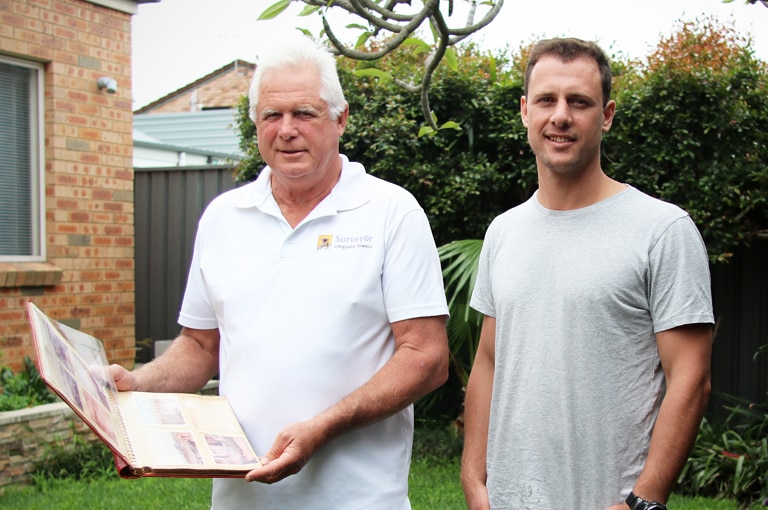 Ken Holloway and Chanan Clark stand in a backyard with Ken holding a photo album.