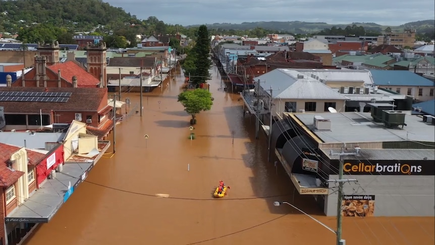 Two men kayak down a flooded street where water reaches halfway up buildings