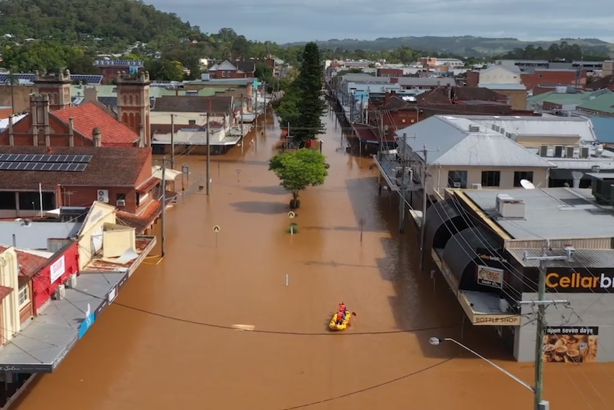 Two men kayak down a flooded street where water reaches halfway up buildings