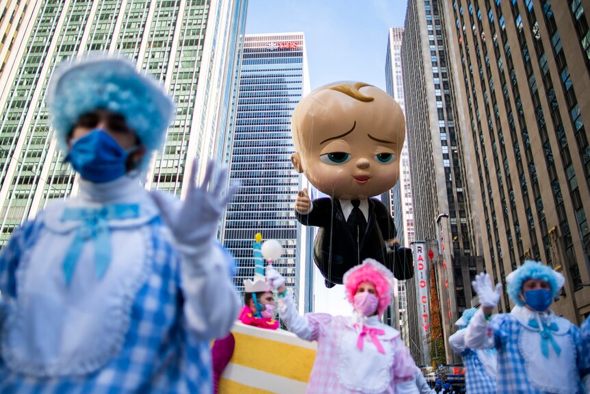An inflatable cartoon baby floats above a adults dressed as babies in a New York Parade