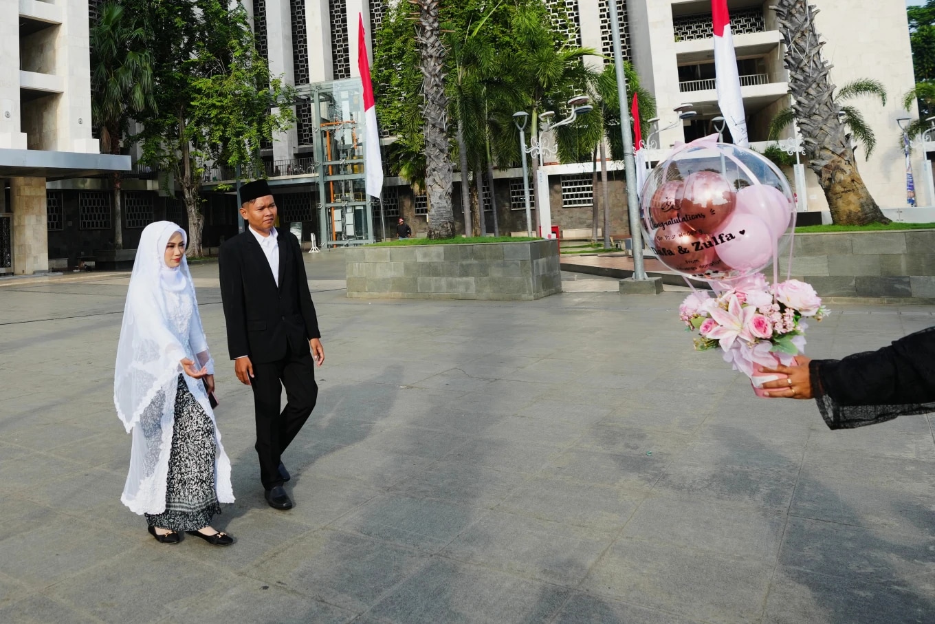 Una mujer vestida de blanco y un hombre de negro caminan hacia un globo con sus nombres escritos.
