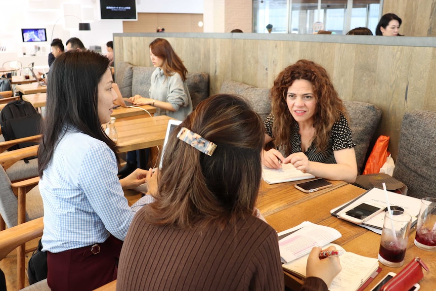 Ms Banaros at a cafe table speaking with two people