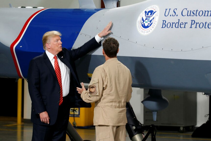 Donald Trump puts his hand on a drone aircraft marked with "US Customs and Border Protection"