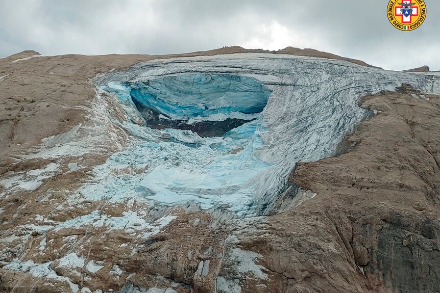 A blue glacier in the middle of a brown mountain.
