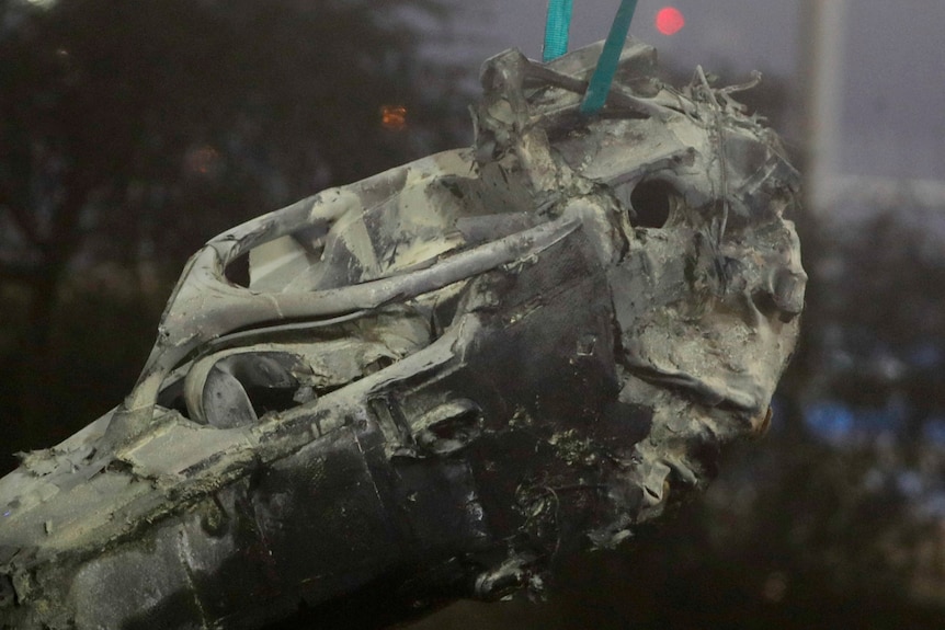 The heavily burnt body of a Formula 1 car hangs from a crane.