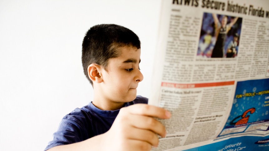 A young boy holds up a newspaper.
