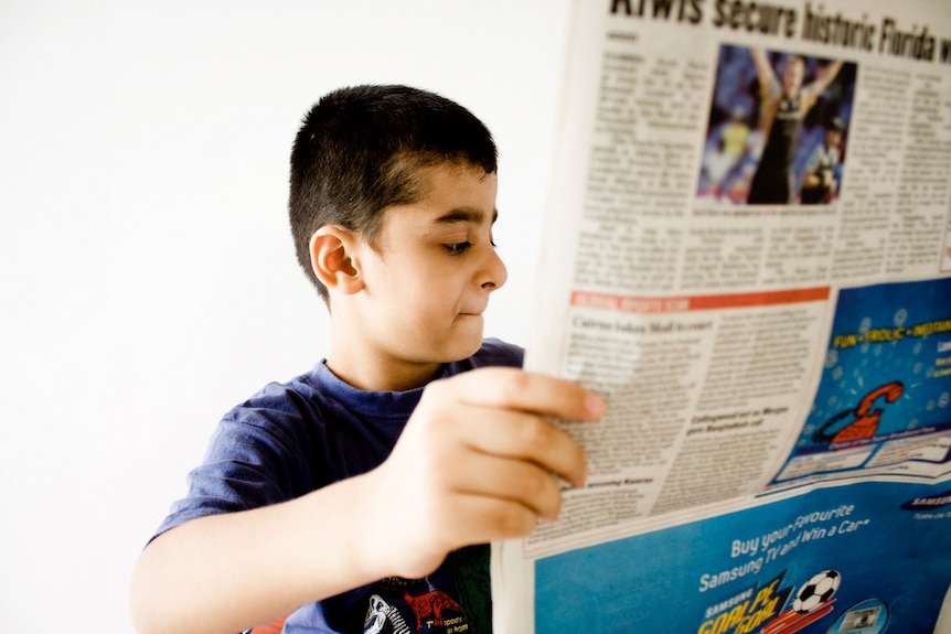 A young boy holds up a newspaper.