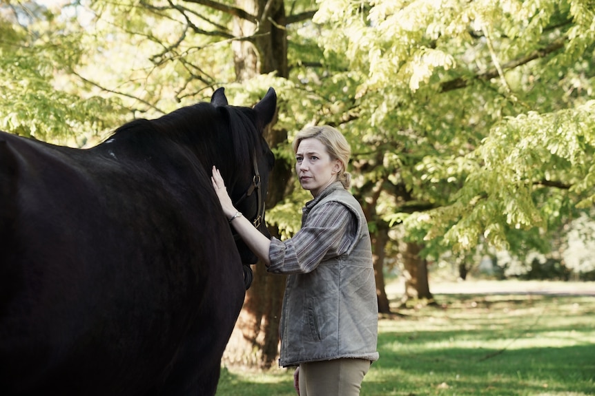 Carrie Coon pats a horse, looking concerned, in the film The Nest