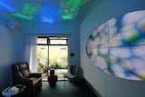 The inside of a hospital room with an armchair and a projection of a blue and green abstract design on the wall