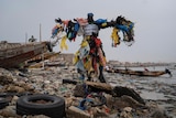 Modou Fall stands in his plastic man costume with his arms outstretched on a beach covered in plastic 