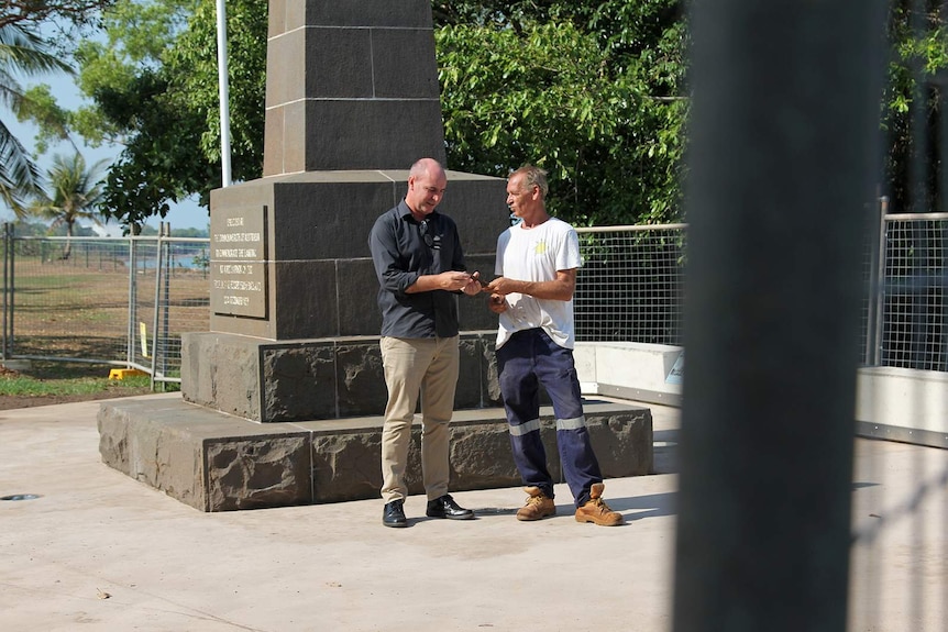 A photo of Clayton Dwyer and Michael Wells comparing the ageing chisel in front of a cenotaph.
