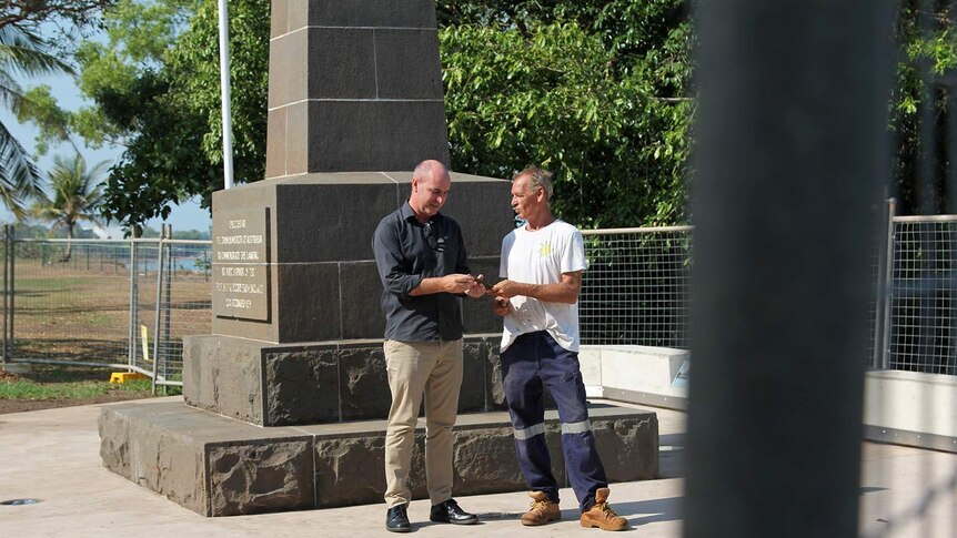 A photo of Clayton Dwyer and Michael Wells comparing the ageing chisel in front of a cenotaph.