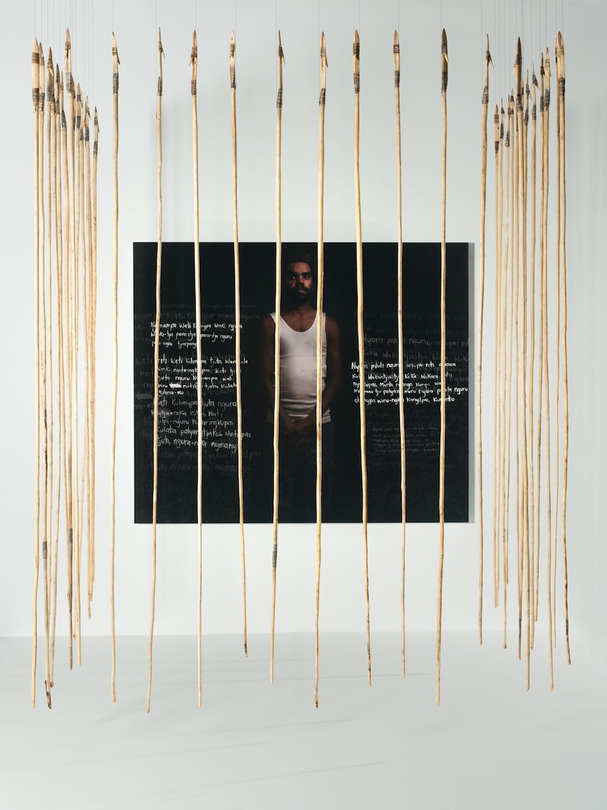 A photograph of a young Aboriginal man caged by suspended spears
