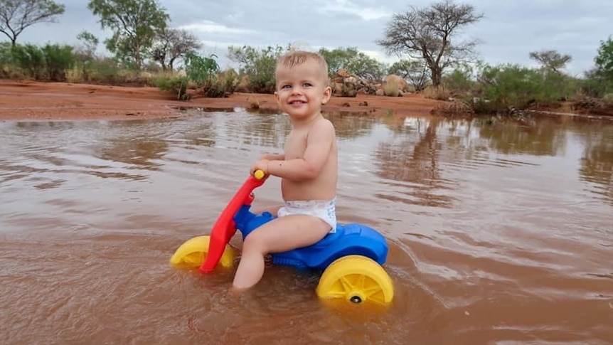 Young boy riding trike through floodwater in outback
