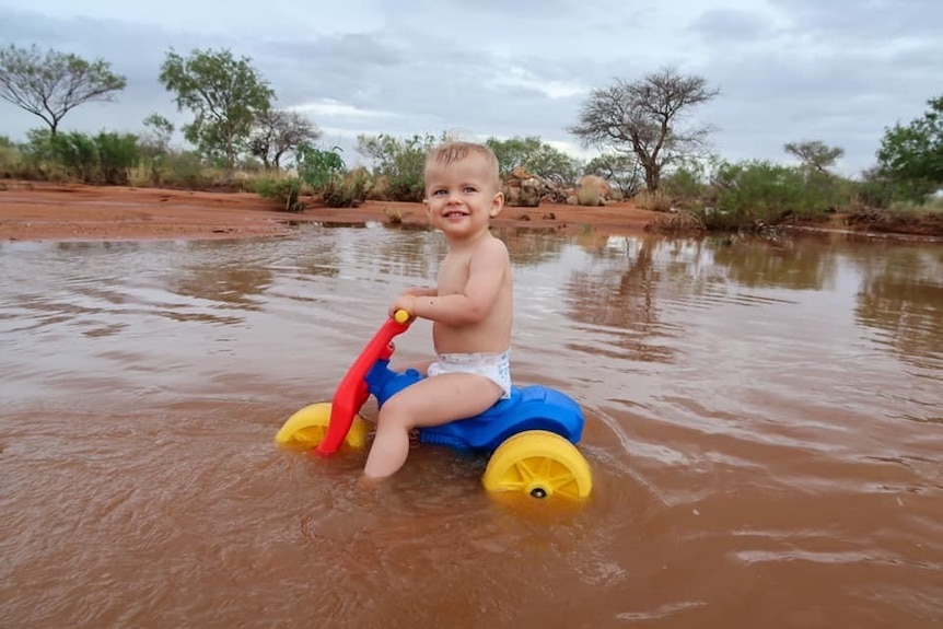 Young boy riding trike through floodwater in outback
