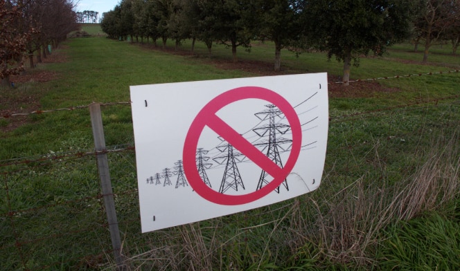sign with red cross over transmission lines and towers on farm gate fence