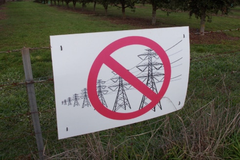 sign with red cross over transmission lines and towers on farm gate fence