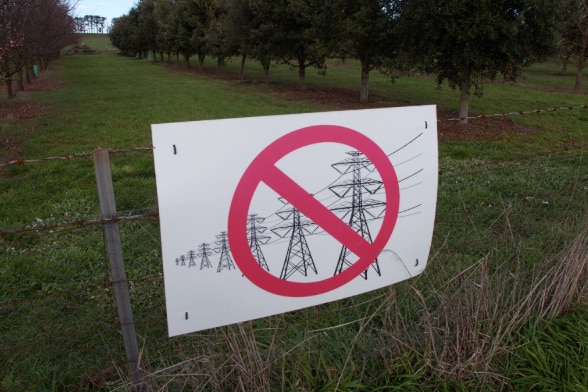 sign with red cross over transmission lines and towers on farm gate fence