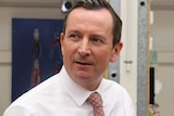 Mark McGowan wearing a white shirt and dark salmon tie, looking away from the camera with a slight smile.