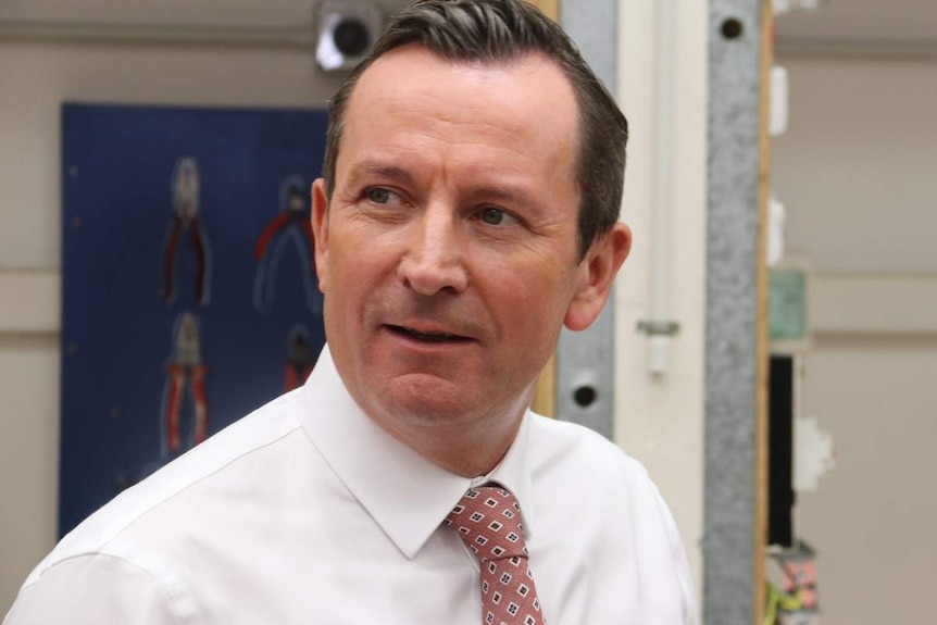 Mark McGowan wearing a white shirt and dark salmon tie, looking away from the camera with a slight smile.