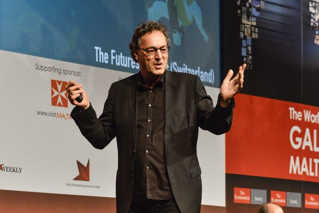 A man gesticulates with his hands while presenting at a conference.