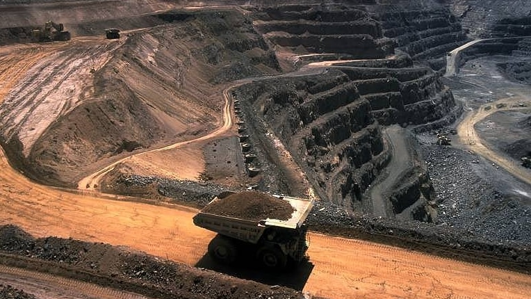 An aerial shot of an open cut coal mine, with a large truck transporting a pile of coal out up a dirt road.