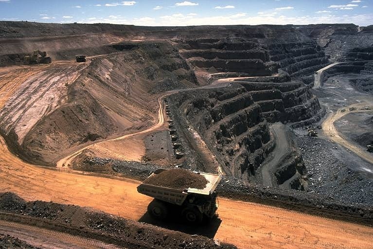 An aerial shot of an open cut coal mine, with a large truck transporting a pile of coal out up a dirt road.