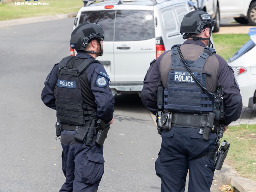 Two police officers in tactical gear stand on a street with their backs to the camera