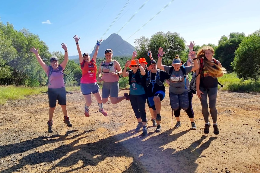 Walkers on a dirt track with mountain in background, jumping with hands in air