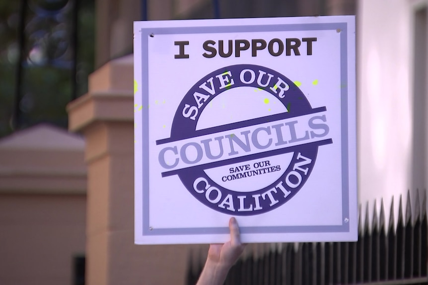 A person holds a sign that reads 'I support the save our councils coalition'