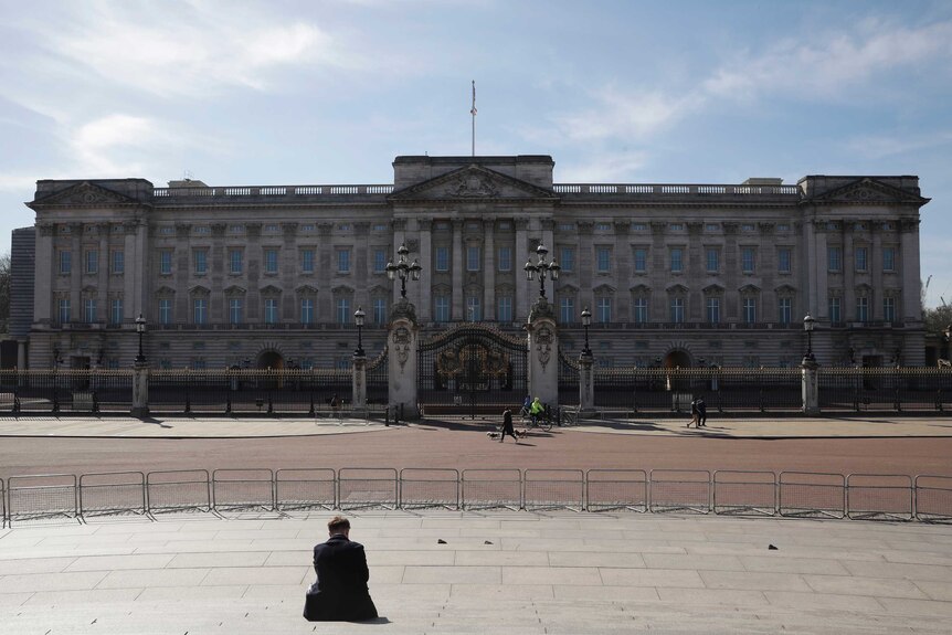 A man sits outside Buckingham Palace alone