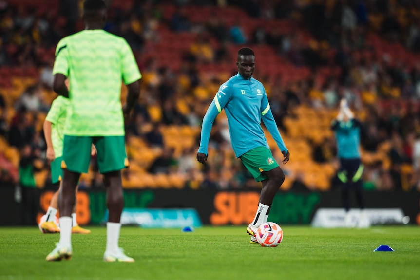 Two soccer players wearing green and blue kick a ball around in a stadium