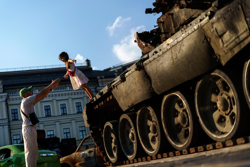 A young girl falls into her father's arms off a Russian tank that was destroyed.