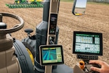 lookimg from inside of a tractor cbin showing a steering wheel and two computer screens.