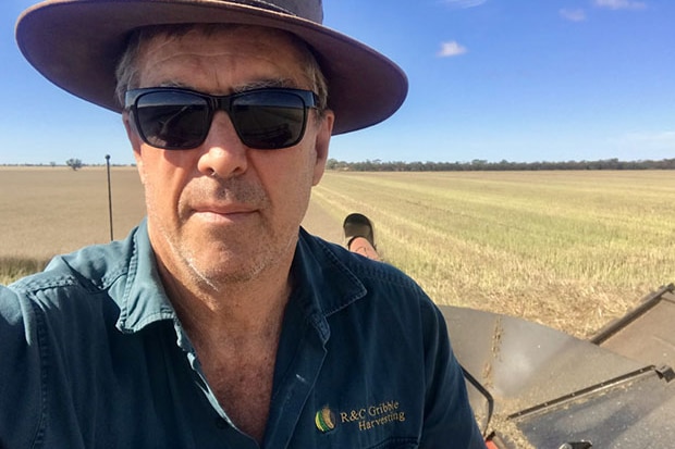 man in hat and glasses sits on a tractor in a paddock